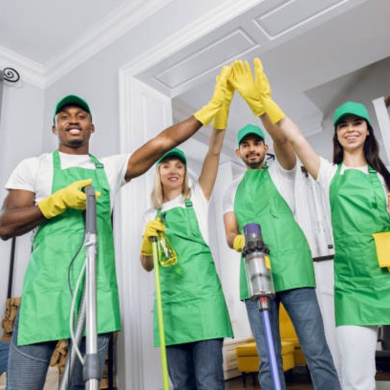 Professional team of mixed race cleaners giving high five, smiling and looking at camera. Happy male and female janitors in uniform finished regular cleanup of modern house.